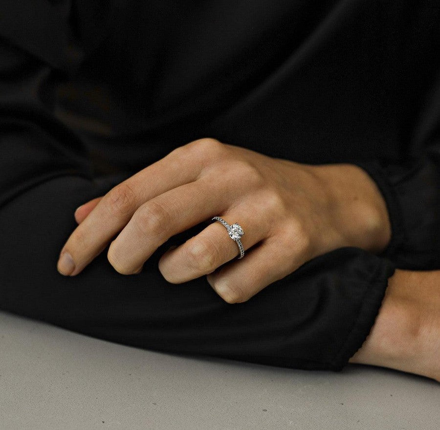 white gold diamond engagement ring with round centre diamond with 4 claws and diamonds claw set in the band on a woman wearing black