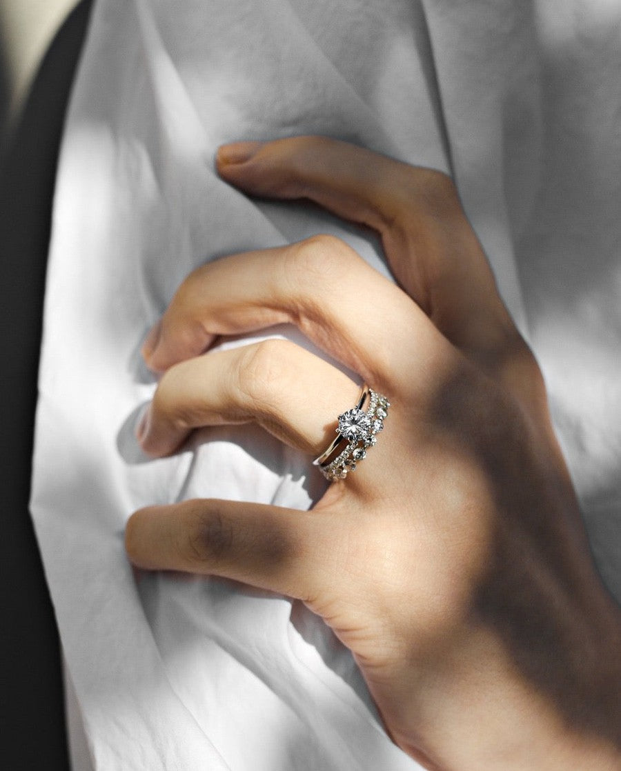white gold round solitaire engagement ring with a diamond wedding ring with single claws on a woman with a white shirt