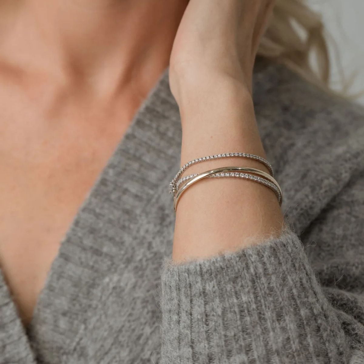 Diamond tennis bracelets and bangles stacked on wrist in grey knit sweater showcasing everyday luxury