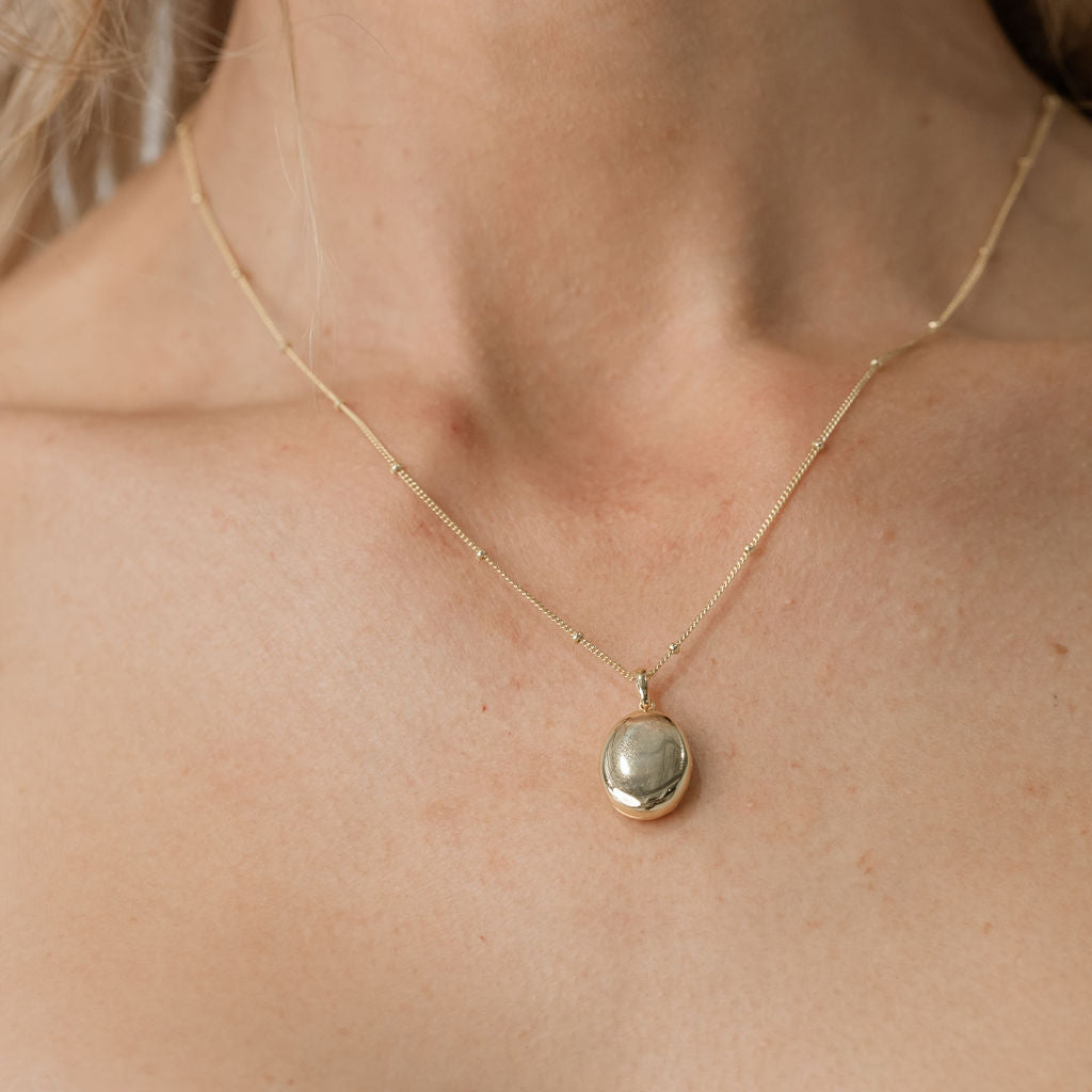 model wearing bead chain necklace with gold oval pendant