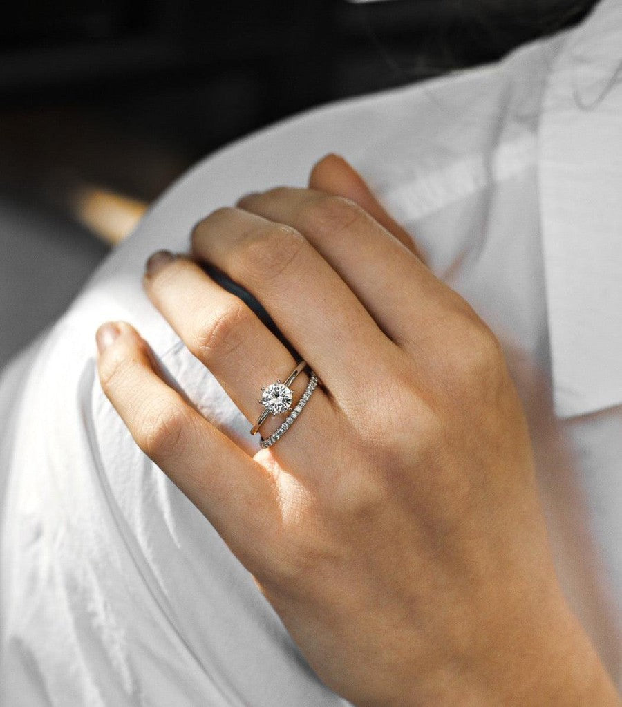 White gold round solitaire engagement ring with diamond wedding ring on a woman with a white shirt