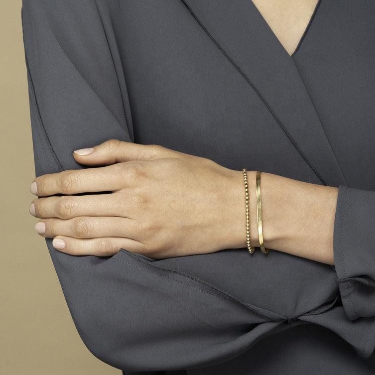 Woman wearing gold herringbone bracelet and gold mini ball bracelet